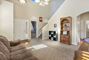 Living room featuring baseboards, arched walkways, light colored carpet, a towering ceiling, and stairway