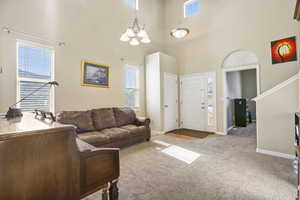 Carpeted living room featuring visible vents, a notable chandelier, a towering ceiling, and baseboards