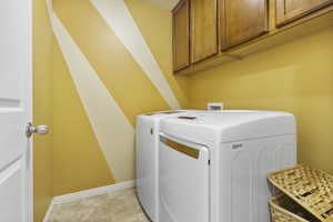 Washroom featuring washing machine and dryer, cabinet space, and baseboards