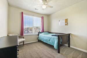 Carpeted bedroom with a ceiling fan, visible vents, baseboards, and a textured ceiling