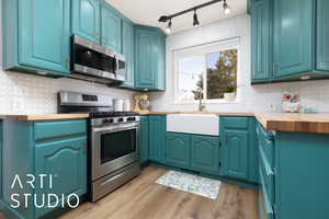 Kitchen featuring butcher block countertops, appliances with stainless steel finishes, blue cabinets, light wood-type flooring, and a sink