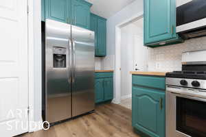 Kitchen with appliances with stainless steel finishes, light wood-type flooring, blue cabinets, and decorative backsplash