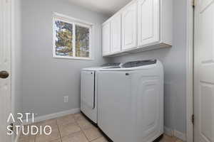 Washroom with light tile patterned flooring, washing machine and clothes dryer, cabinet space, and baseboards