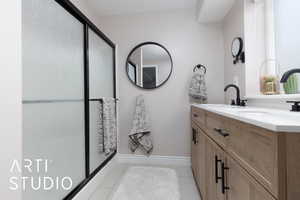 Bathroom featuring a shower with shower door, vanity, baseboards, and tile patterned floors