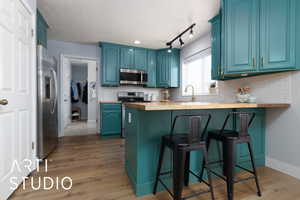 Kitchen with a breakfast bar, a peninsula, stainless steel appliances, blue cabinetry, and wooden counters