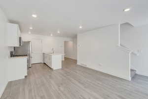 Kitchen with a sink, visible vents, white cabinetry, open floor plan, and light countertops