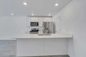 Kitchen with a peninsula, stainless steel appliances, light countertops, white cabinetry, and a sink