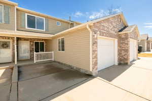 View of side of property with an attached one car garage, covered porch, and brick siding, extra guest parking right close to the unit.