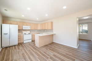 Kitchen featuring a peninsula for bar stool seating ,New LVP flooring  white appliances, light countertops, and light  wood cabinetry.