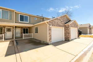 View of property featuring a one car garage, brick siding, driveway, and partially fenced porch. Also provides for guest parking.