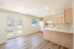 Kitchen with simi formal dining area light countertops, light wood cabinets, white appliances, and a peninsula which allows for bar stool seating.