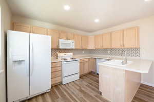 Kitchen featuring a peninsula for bar stool seating ,New LVP flooring  white appliances, light countertops, and light brown cabinetry.