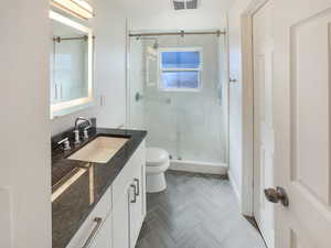Full bathroom with a marble finish shower, toilet, visible vents, baseboards, and vanity