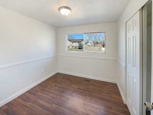 Unfurnished bedroom with dark wood-type flooring, a textured ceiling, and visible vents