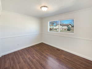 Empty room with wood finished floors, visible vents, ornamental molding, baseboards, and a textured ceiling