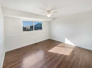 Empty room featuring a wainscoted wall, visible vents, dark wood-type flooring, a ceiling fan, and a textured ceiling