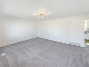 Spare room featuring light colored carpet, ornamental molding, and visible vents