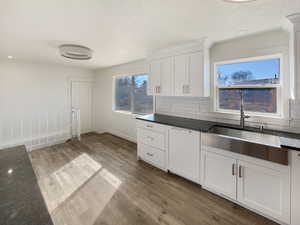 Kitchen featuring backsplash, light wood-style floors, white cabinets, a sink, and dark stone countertops