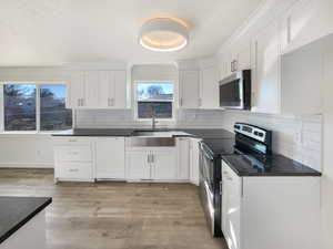 Kitchen with stainless steel appliances, backsplash, light wood-style floors, white cabinets, and a sink