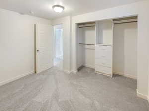 Unfurnished bedroom featuring a closet, baseboards, and light carpet