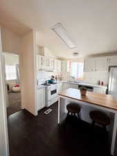 Kitchen with under cabinet range hood, white range with gas stovetop, white cabinets, vaulted ceiling, and light countertops