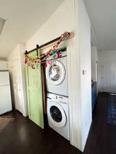 Laundry room featuring stacked washer and dryer, dark wood-style flooring, and laundry area