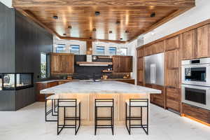 Kitchen with marble finish floor, a breakfast bar area, light countertops, stainless steel double oven, and a kitchen island with sink