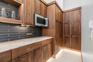 Kitchen with light stone counters, marble finish floor, brown cabinets, stainless steel microwave, and backsplash