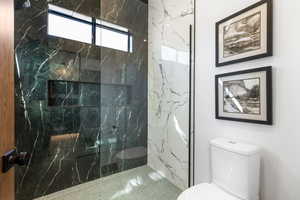 Full bathroom featuring toilet and a marble finish shower