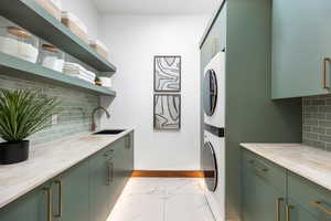 Washroom with marble finish floor, cabinet space, a sink, stacked washing maching and dryer, and baseboards