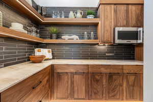 Kitchen with light countertops, stainless steel microwave, backsplash, and brown cabinetry