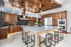 Kitchen with marble finish floor, stainless steel appliances, hanging light fixtures, and an island with sink