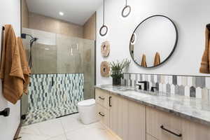 Bathroom featuring toilet, a tile shower, backsplash, and vanity