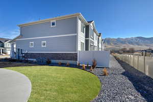 View of property exterior featuring stone siding, a lawn, fence, and a mountain view