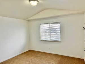 Carpeted empty room with lofted ceiling, a textured ceiling, and baseboards