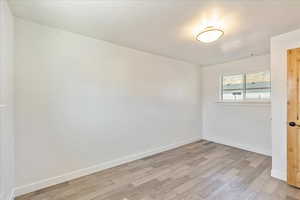 Empty room with visible vents, light wood-style flooring, and baseboards