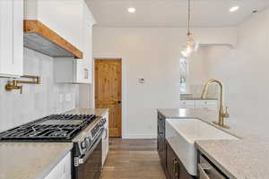 Kitchen featuring stainless steel appliances, white cabinetry, decorative light fixtures, and light stone counters