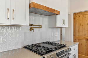 Kitchen featuring stainless steel gas range, white cabinetry, light countertops, and decorative backsplash