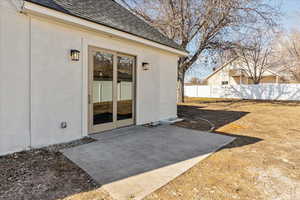 Property entrance with a patio area, a shingled roof, fence, and brick siding