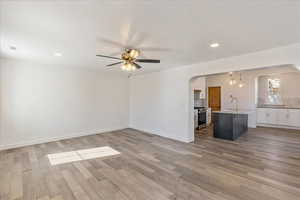 Unfurnished living room featuring arched walkways, light engineered hard wood-style flooring, and a sink