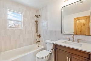 Full bath with tile walls, bathing tub / shower combination, visible vents, toilet, and vanity