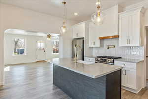 Kitchen featuring arched walkways, hanging light fixtures, appliances with stainless steel finishes, and white cabinetry