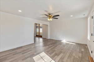 Unfurnished room with light wood-type flooring, ceiling fan, arched walkways, and baseboards