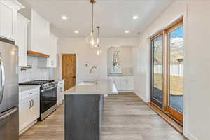 Kitchen featuring a kitchen island with sink, stainless steel appliances, a sink, white cabinetry, and light countertops