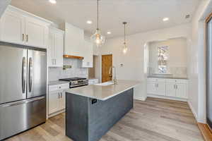 Kitchen featuring a kitchen island with sink, stainless steel appliances, a sink, white cabinets, and light countertops