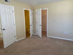 Master bedroom with light carpet, a walk in closet, and master bathroom