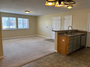 Kitchen featuring a peninsula, a sink, open floor plan, stainless steel dishwasher, and dark carpet