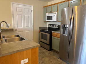 Kitchen with appliances with stainless steel finishes, a sink, and green cabinets