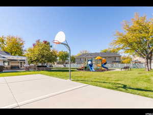 View of basketball court featuring basketball hoop, a lawn, a playground, and fence