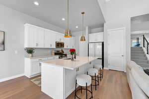 Kitchen with stainless steel appliances, pendant lighting, light countertops, and white cabinetry